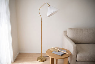Aurelia pleated fabric floor lamp standing beside a sofa in a New Zealand living room with a soft dusting brush and a folded microfibre cloth on the side table
