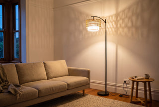 Rattan floor lamp buyer's guide NZ: the Rousseau woven paper rope floor lamp switched on beside a linen sofa in an Auckland villa lounge at dusk, weave pattern on the wall