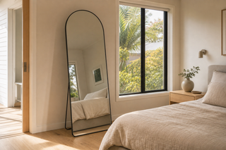 Mirrors Auckland — the Titan black arched full-length mirror leaning in a warm Auckland bedroom with a nikau palm through the window
