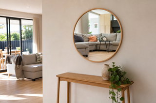 Small wall mirror NZ — a round 100cm Aure wall mirror with a slim oak frame above a narrow timber console in a bright New Zealand living room