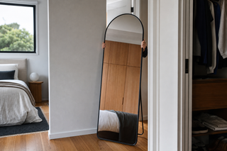 Standing mirror NZ — slim 160cm matte black arched standing mirror being shifted between rooms in a modern Auckland home