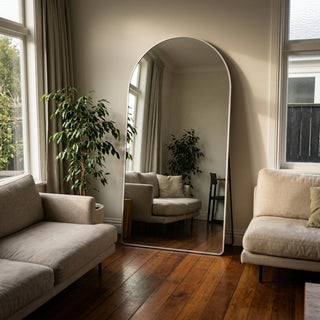 Facet straight-edged full-length mirror with sleek black frame in a minimalist room, reflecting elegant wall paneling and soft lighting from a wall-mounted lamp.