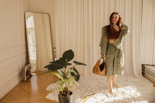 A young woman stands in a minimalist room with a freestanding full-length mirror and bohemian-style decor, highlighting the natural light and earthy tones.
