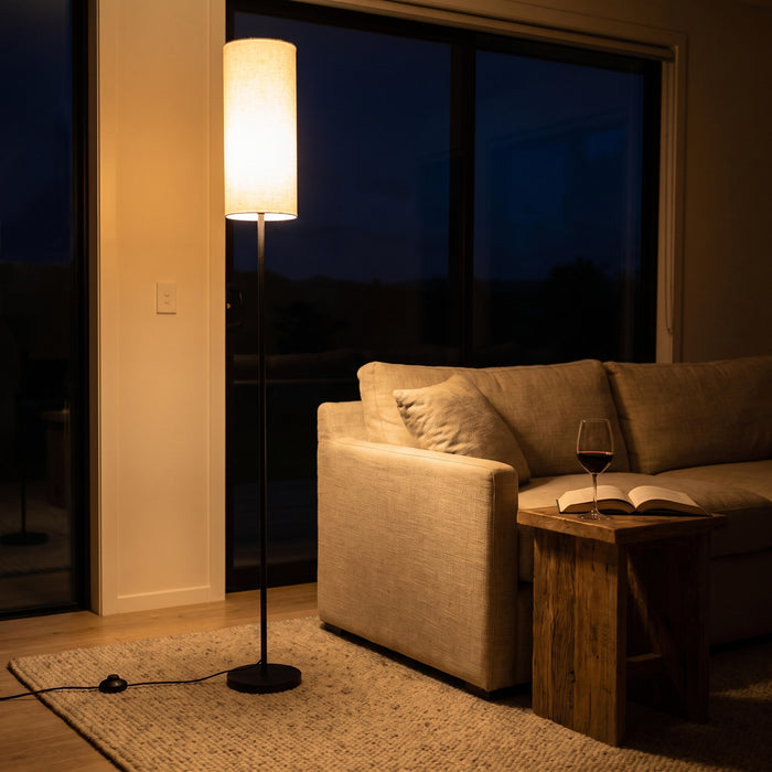 Chandelle Linen Column Floor Lamp switched on in the evening, its linen shade glowing warmly against the night lights of the room