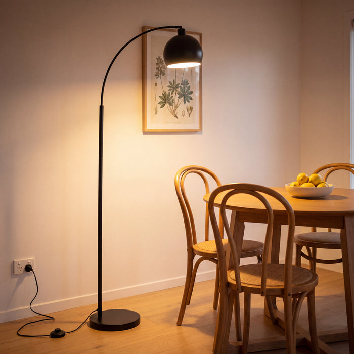 Saturne Black Globe Arc Floor Lamp beside a round oak dining table in the evening
