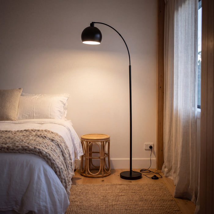 Saturne Black Globe Arc Floor Lamp casting a soft glow beside a bed in a calm bedroom