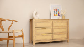 Raya 6-drawer lowboy dresser in natural oak with woven rattan drawer fronts and gold handles, styled in a neutral living room (123 × 40 × 75 cm).