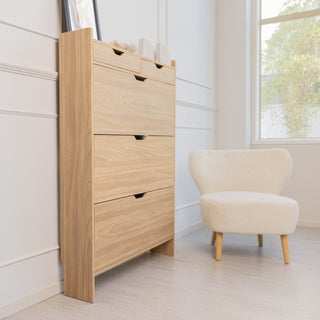 Side angle of the Risa Slim Shoe Cabinet in oak finish, placed beside a cream accent chair and window. The slim design and tall profile highlight its space-saving style, ideal for narrow entryways or modern living spaces.