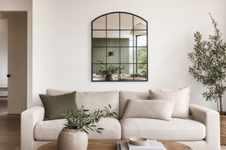 Arched window wall mirror above linen sofa in modern New Zealand lounge